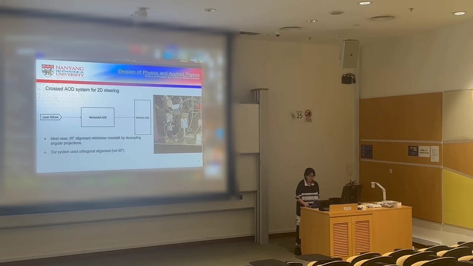 Me at the lectern of a lecture theatre, beside a projected slide titled Crossed AOD system for 2D steering.