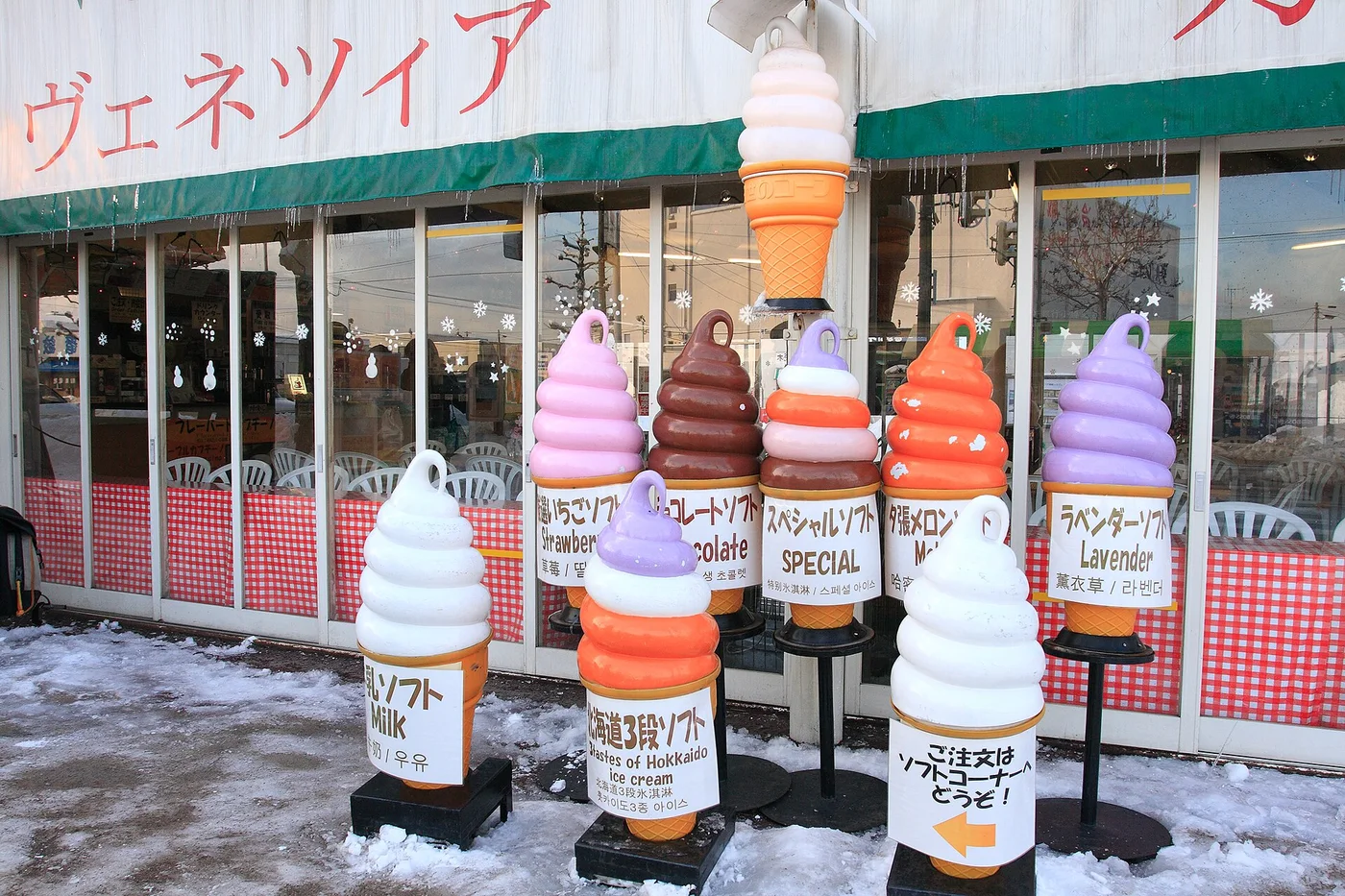 A row of giant model soft-serve cones in flavours such as milk, melon, chocolate and lavender, standing in the snow outside a shop in Otaru.